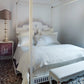 Bedroom with a canopy bed, white bedding, and a bench.