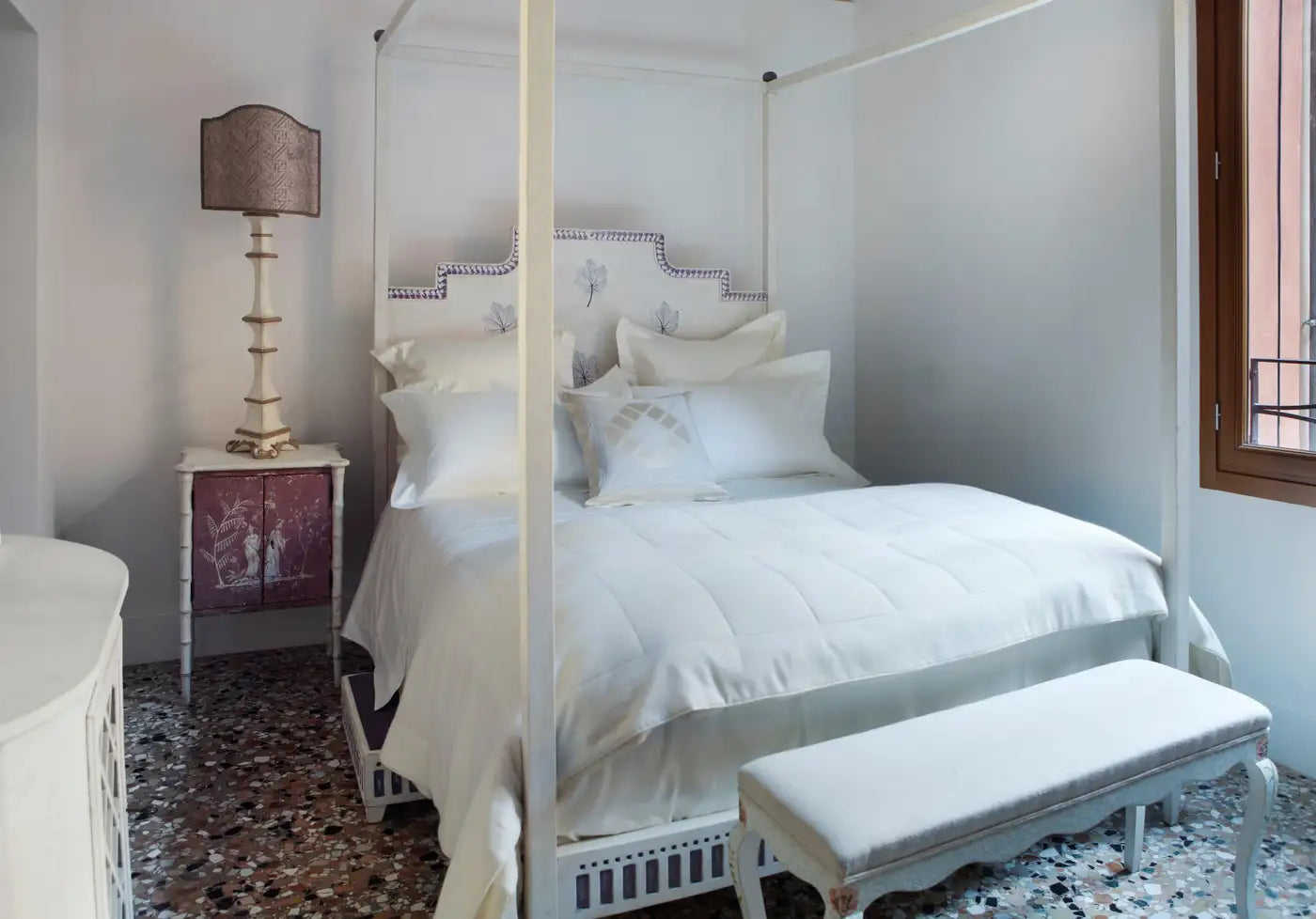 Bedroom with a canopy bed, white bedding, and a bench.