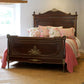 Vintage wooden bed with floral pillows and pink bedding in a room with a window.