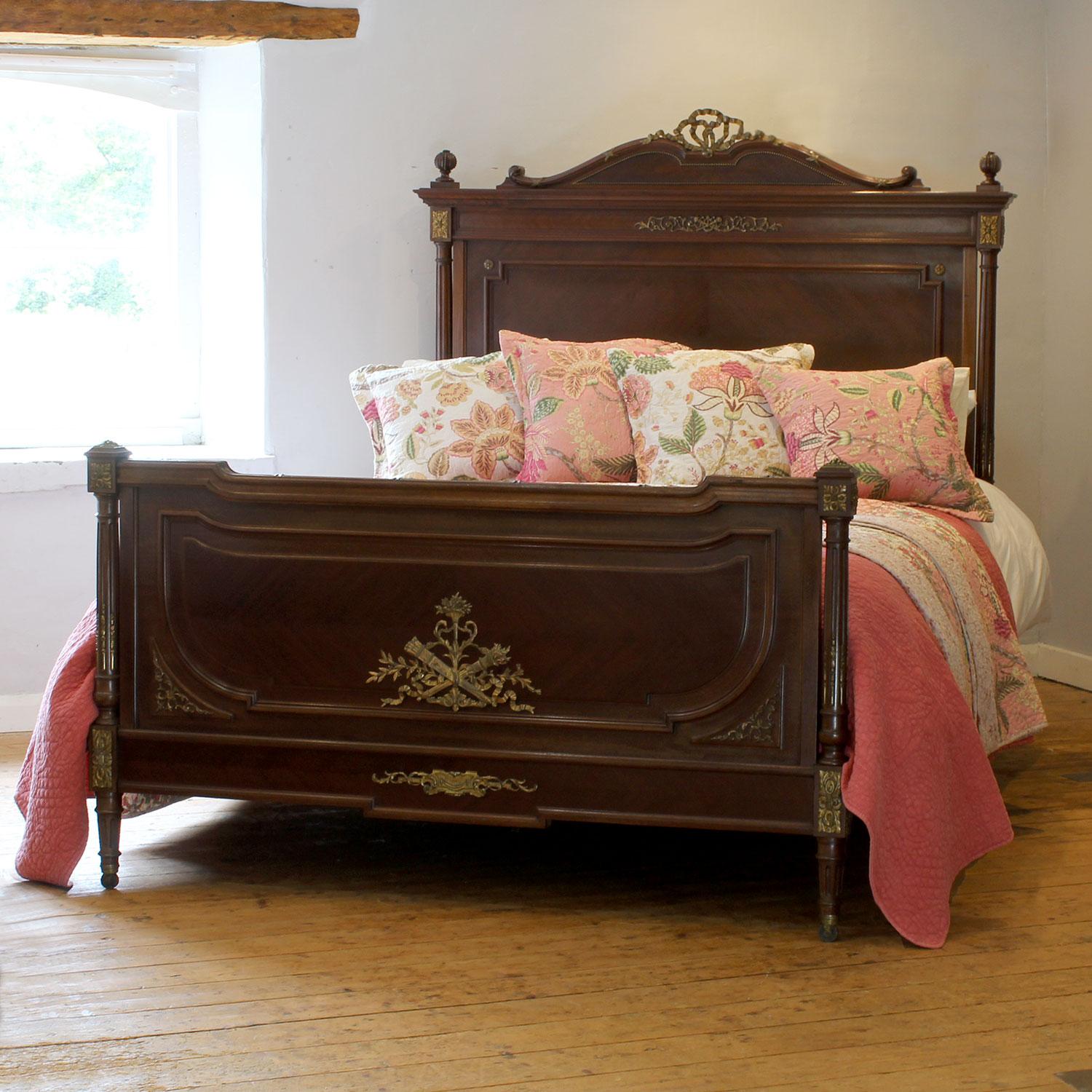 Vintage wooden bed with floral pillows and pink bedding in a room with a window.