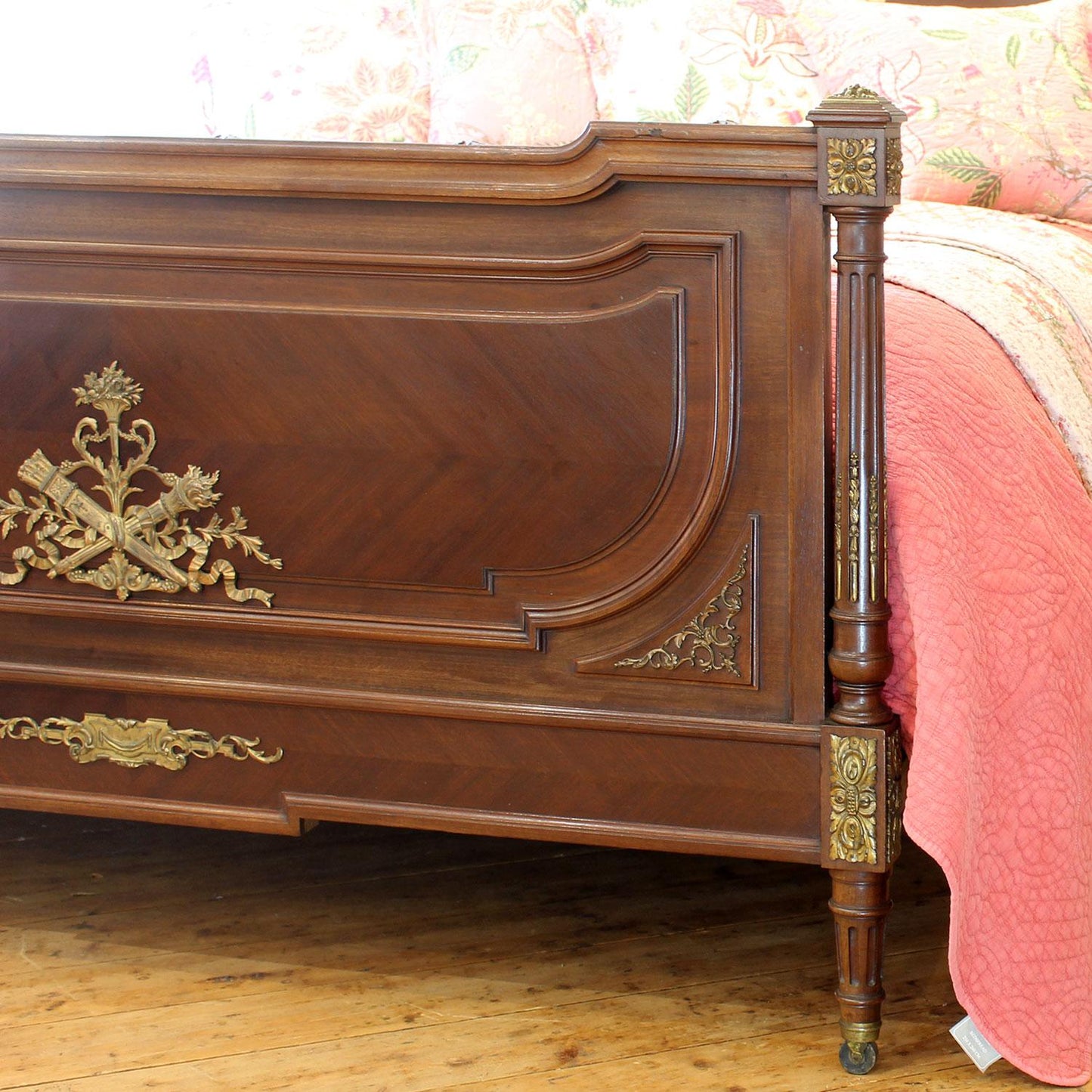 Wooden bed with ornate brass details and pink bedding.