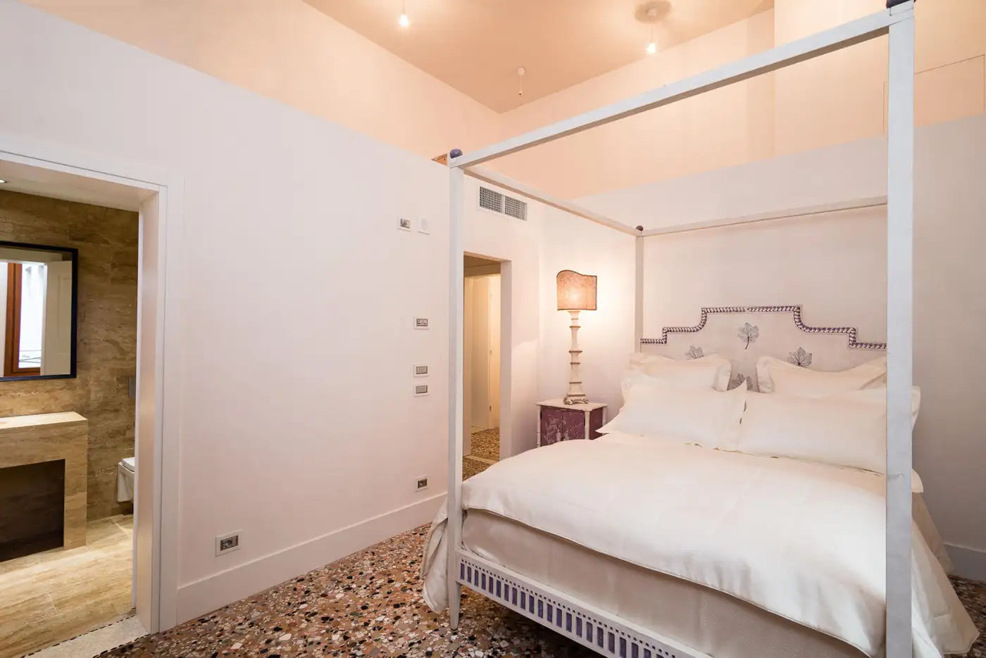 Bedroom with a four-poster bed and a lamp on a nightstand.