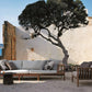 Outdoor seating area with wooden furniture and cushions near a body of water and white wall.