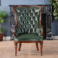 Green leather chair with wooden armrests in a room with a fireplace and plants.