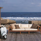 Wooden outdoor sofa with cushions on a deck overlooking the ocean.