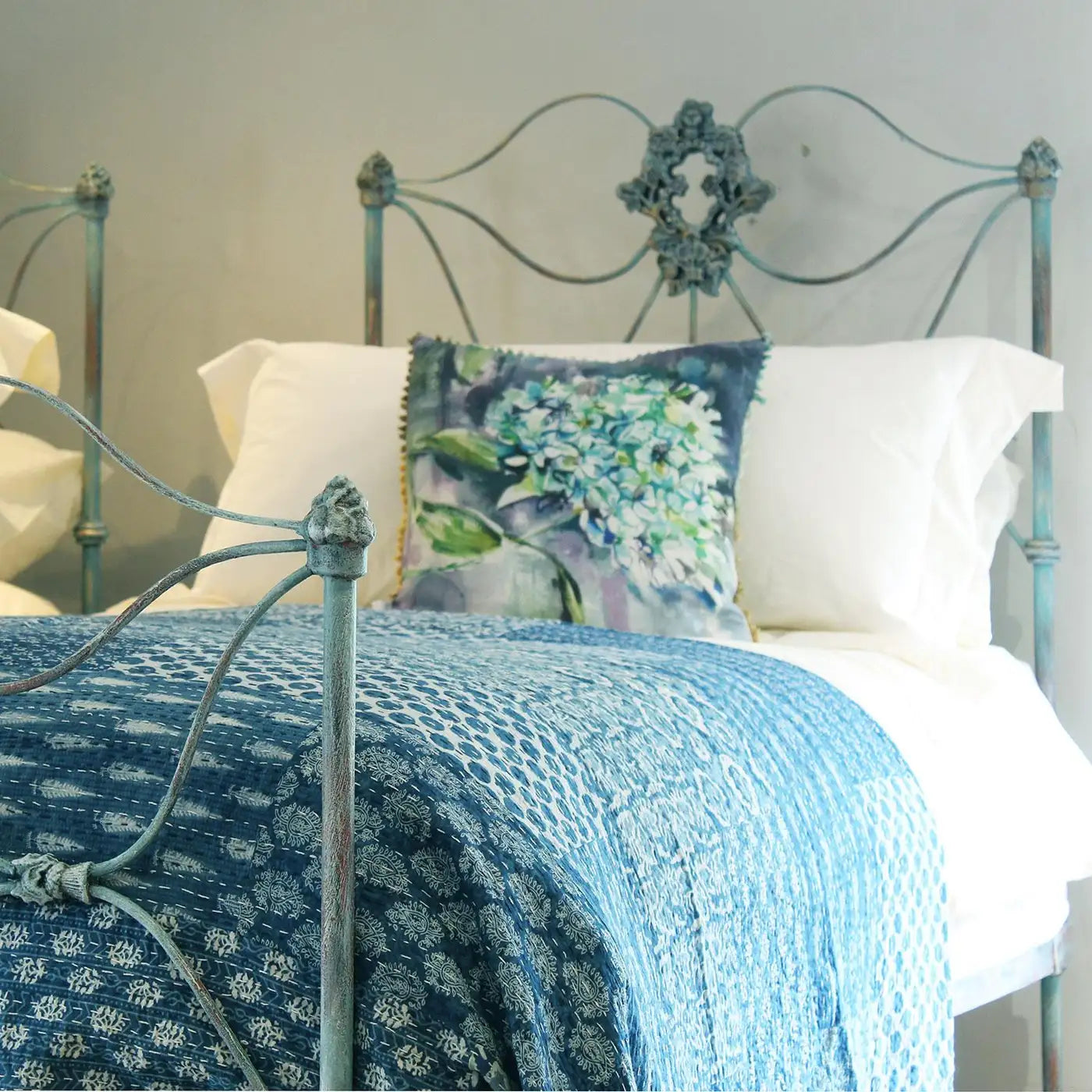 Bed with floral pillows and a blue textured blanket on a metal bedframe.