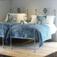 Decorative bed with blue patterned bedding and white pillows on a wooden floor.