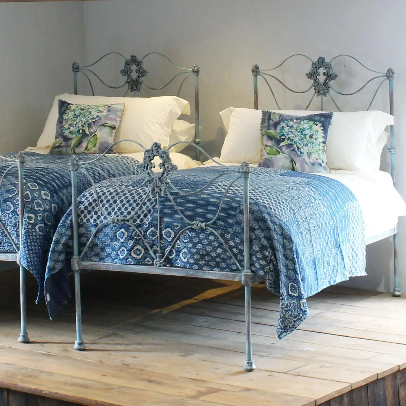 Decorative bed with blue patterned bedding and white pillows on a wooden floor.