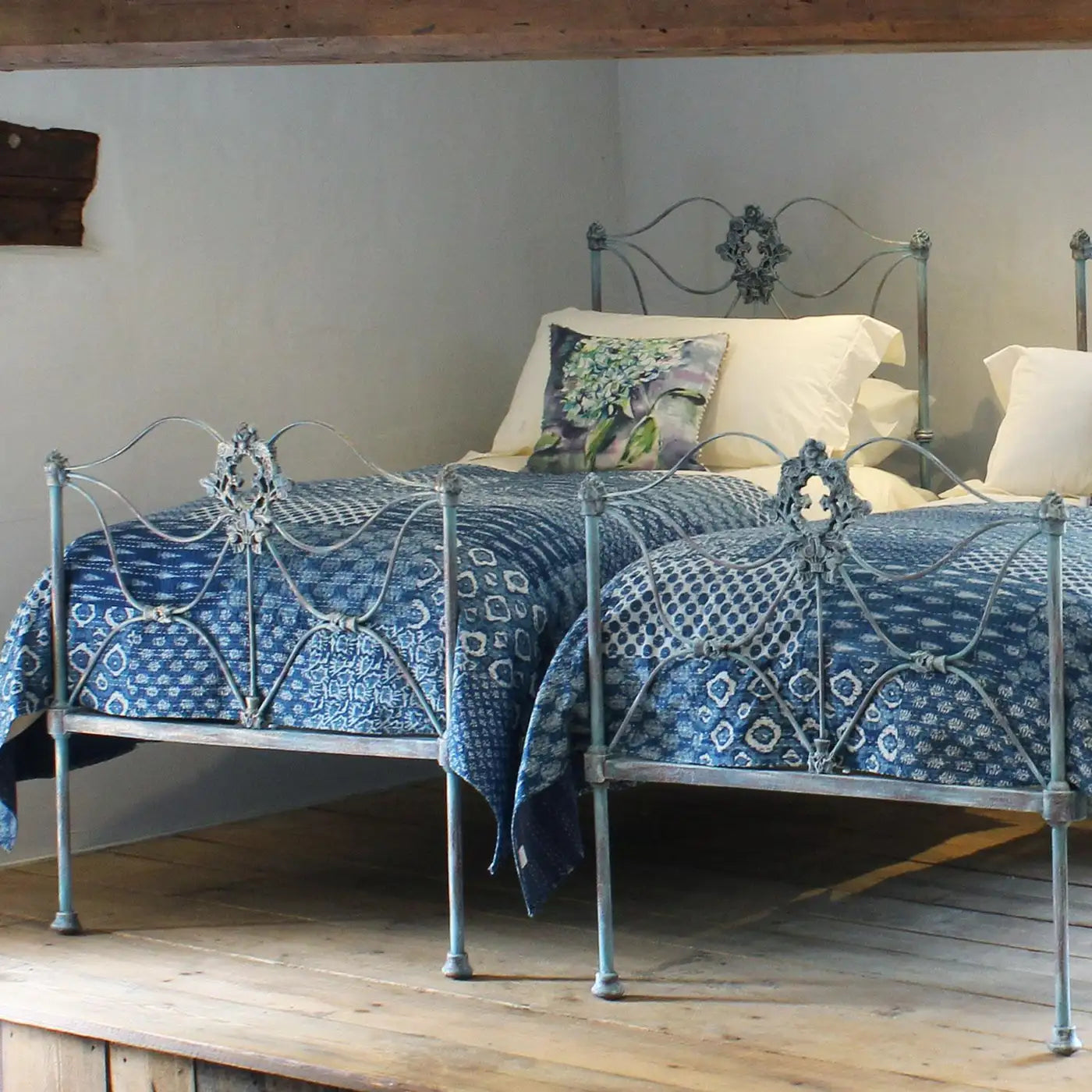 Decorative metal bed with blue patterned bedding in a room with wooden floor and white walls.