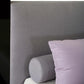 Gray headboard with a cylindrical pillow and a purple pillow on a bed.