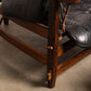 Close-up of a wooden chair with black leather cushion on a concrete floor