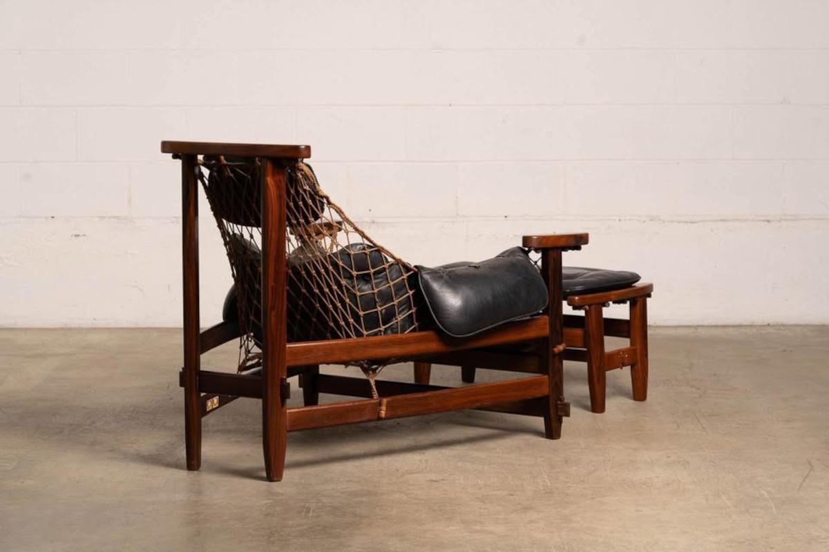 Wooden lounge chair with black cushion on a plain floor and wall background