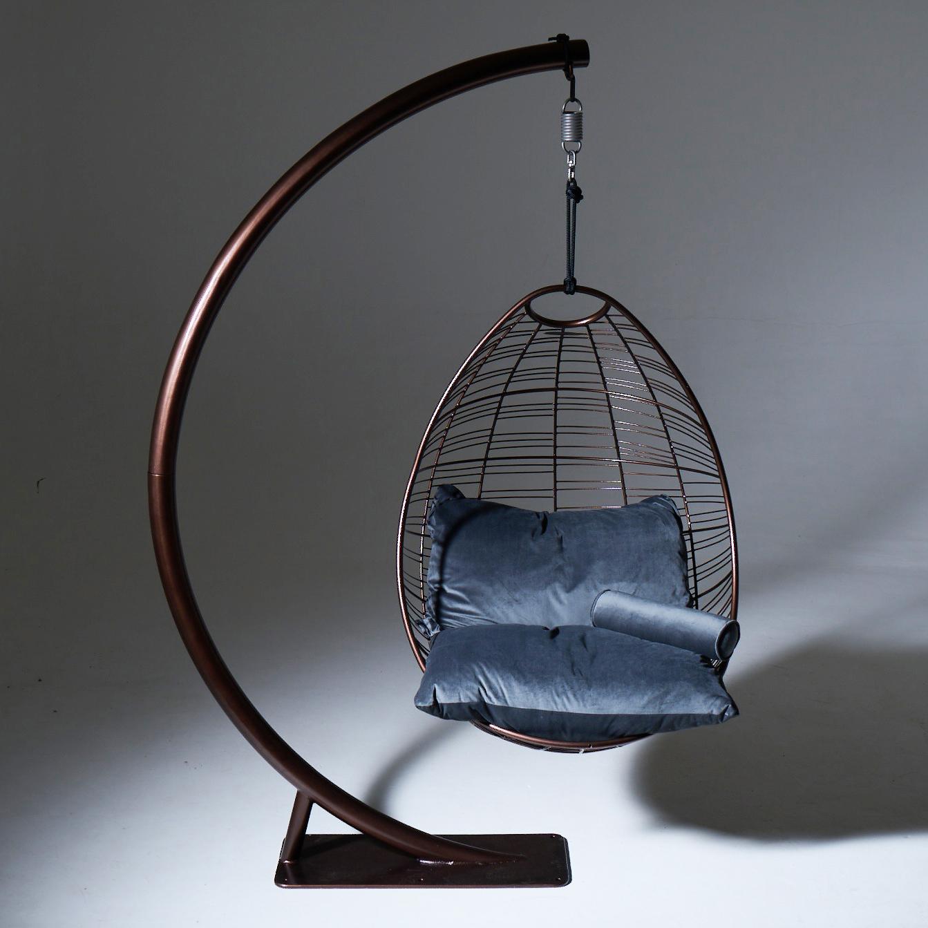 Hanging chair with blue cushions on a dark metal stand against a gray background
