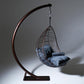Hanging chair with blue cushion on a curved metal stand against a gray background
