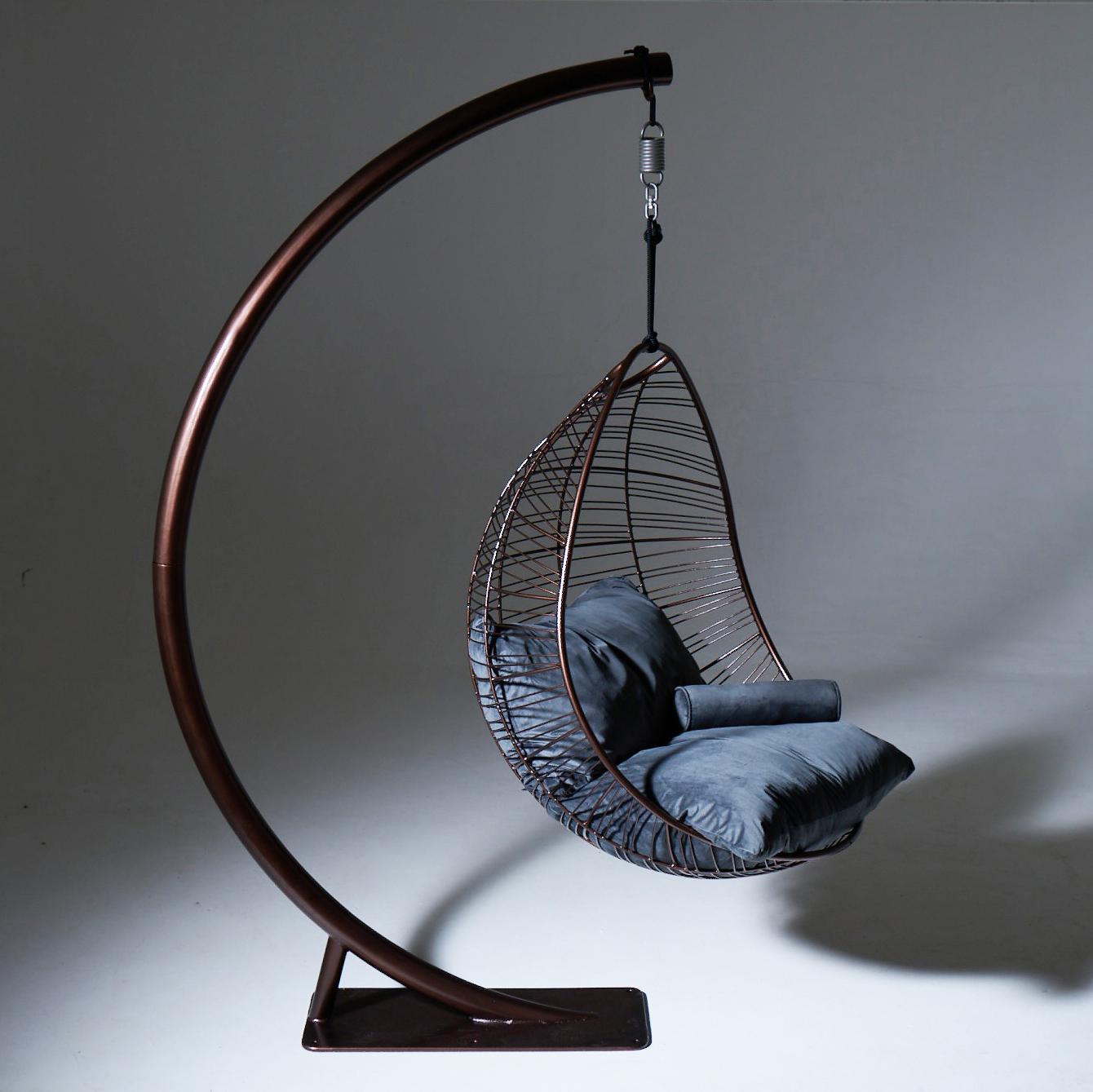 Hanging chair with blue cushion on a curved metal stand against a gray background