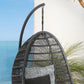 Gray woven hanging chair with a cushion against a blue wall and plant