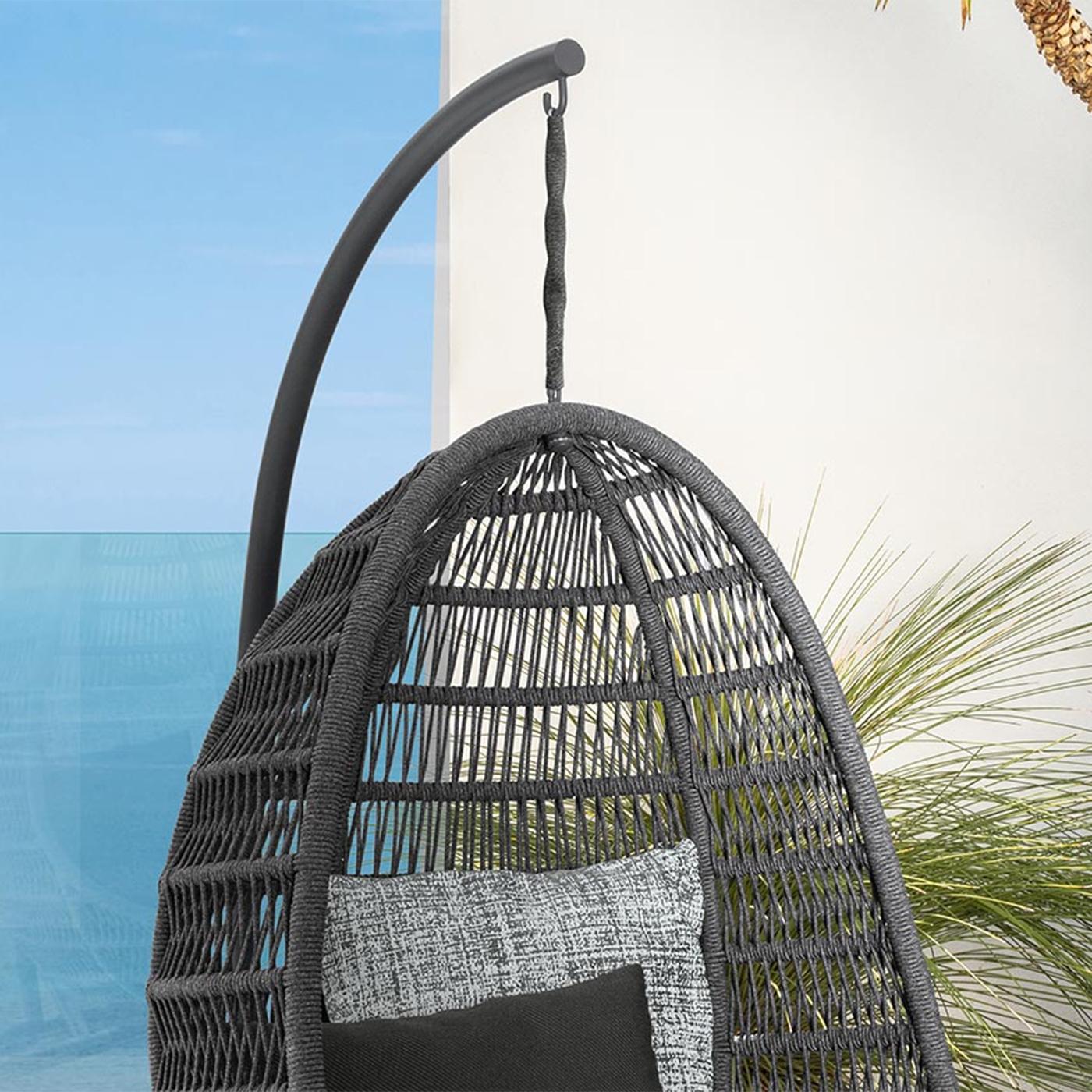 Gray woven hanging chair with a cushion against a blue wall and plant