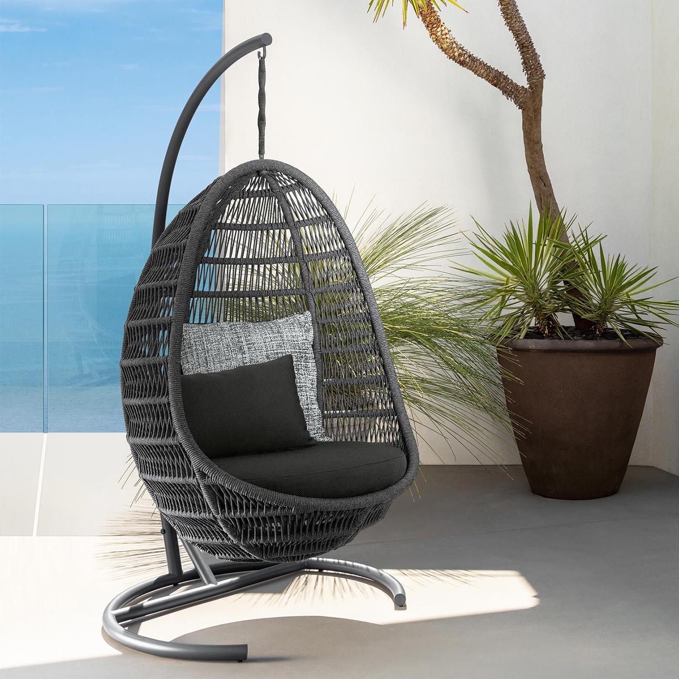 Black wicker egg chair with cushions on a patio with plants and a blue wall.