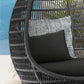 Wicker chair with black and gray cushions against a blurred natural background
