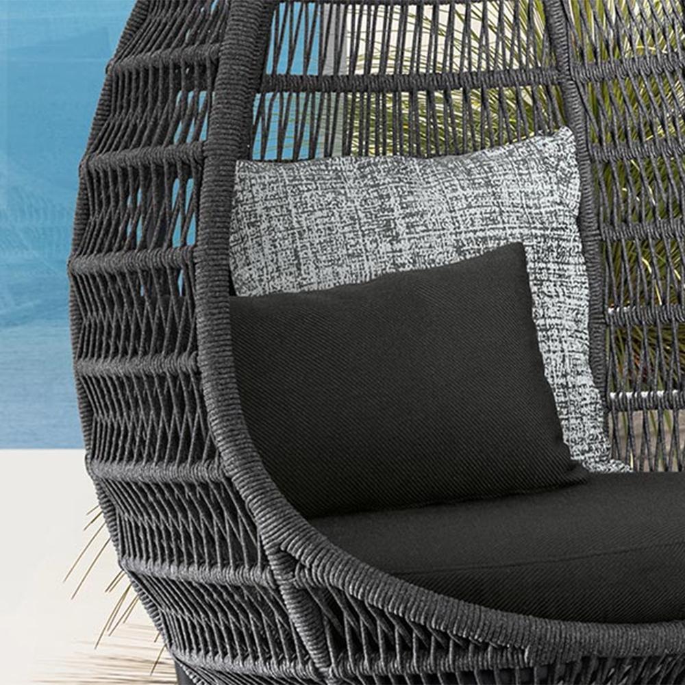 Wicker chair with black and gray cushions against a blurred natural background