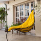 Yellow hammock chair in a patio area with plants and a building in the background