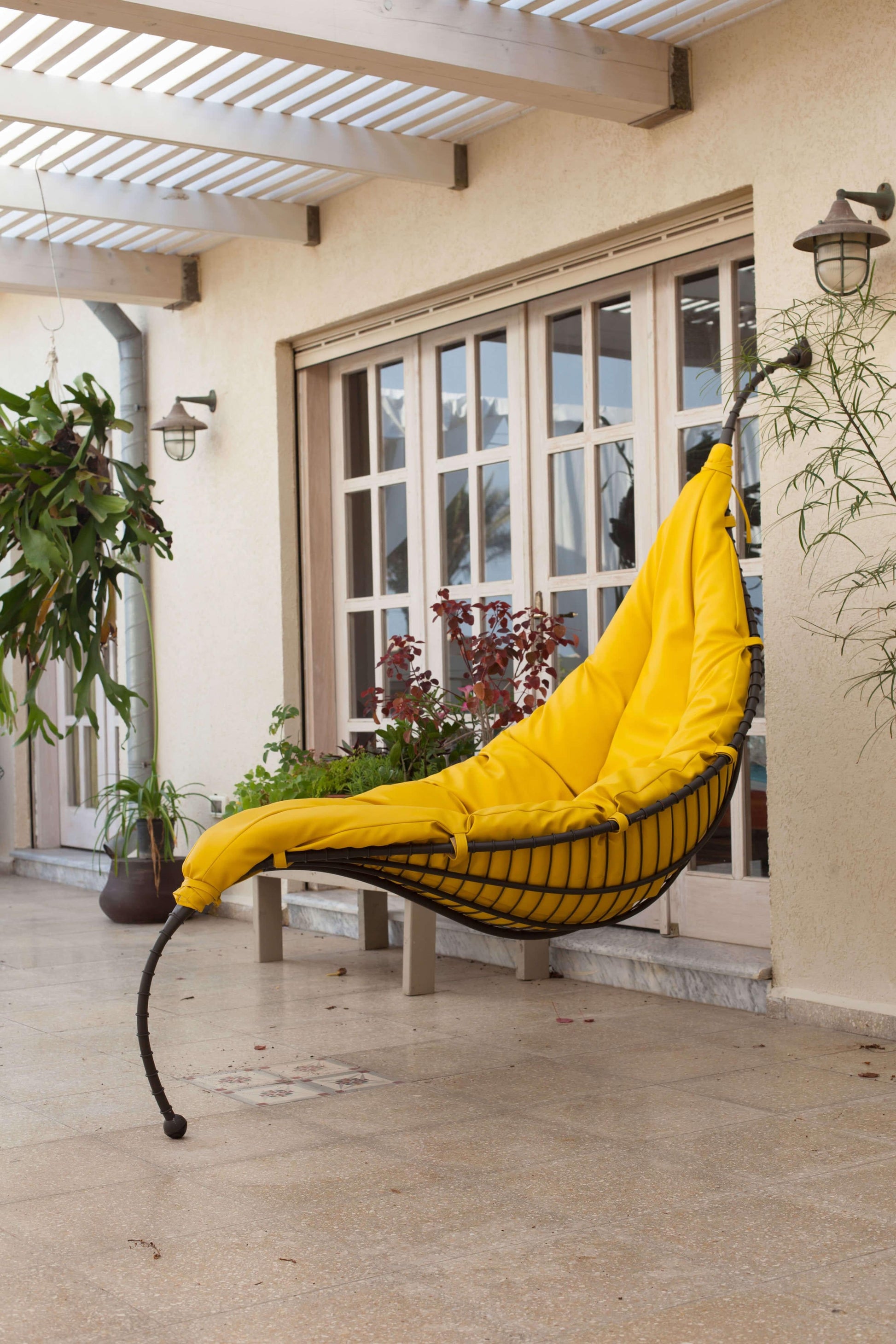Yellow hammock chair in a patio area with plants and a building in the background