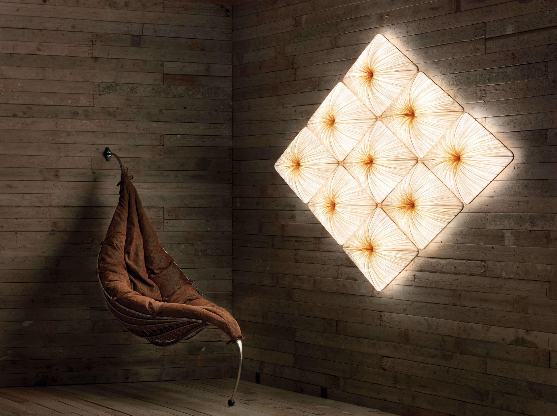 Wall-mounted light fixture casting a warm glow on a wooden wall with a hanging chair.