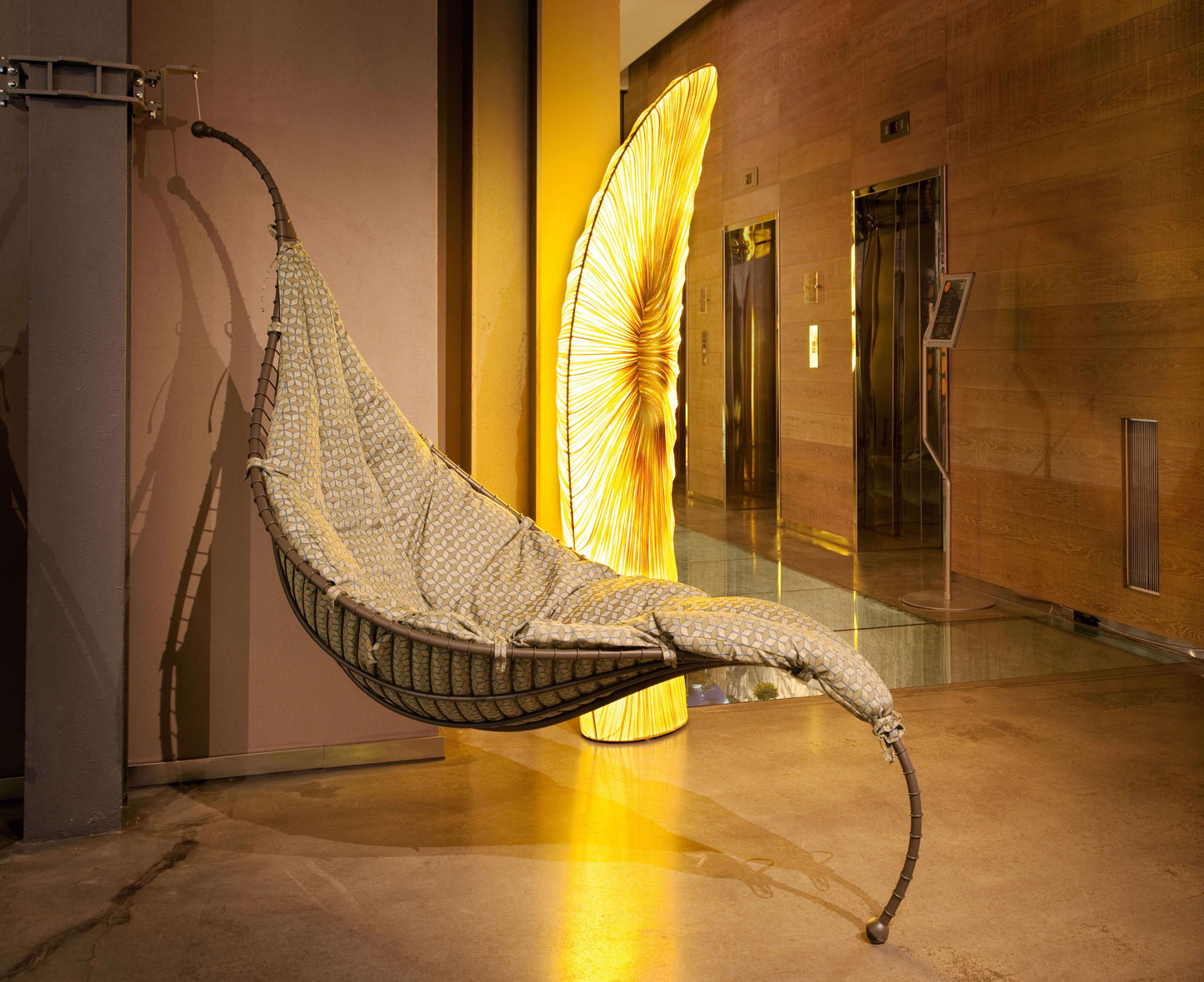Hanging chair in a modern indoor setting with a large decorative light in the background.
