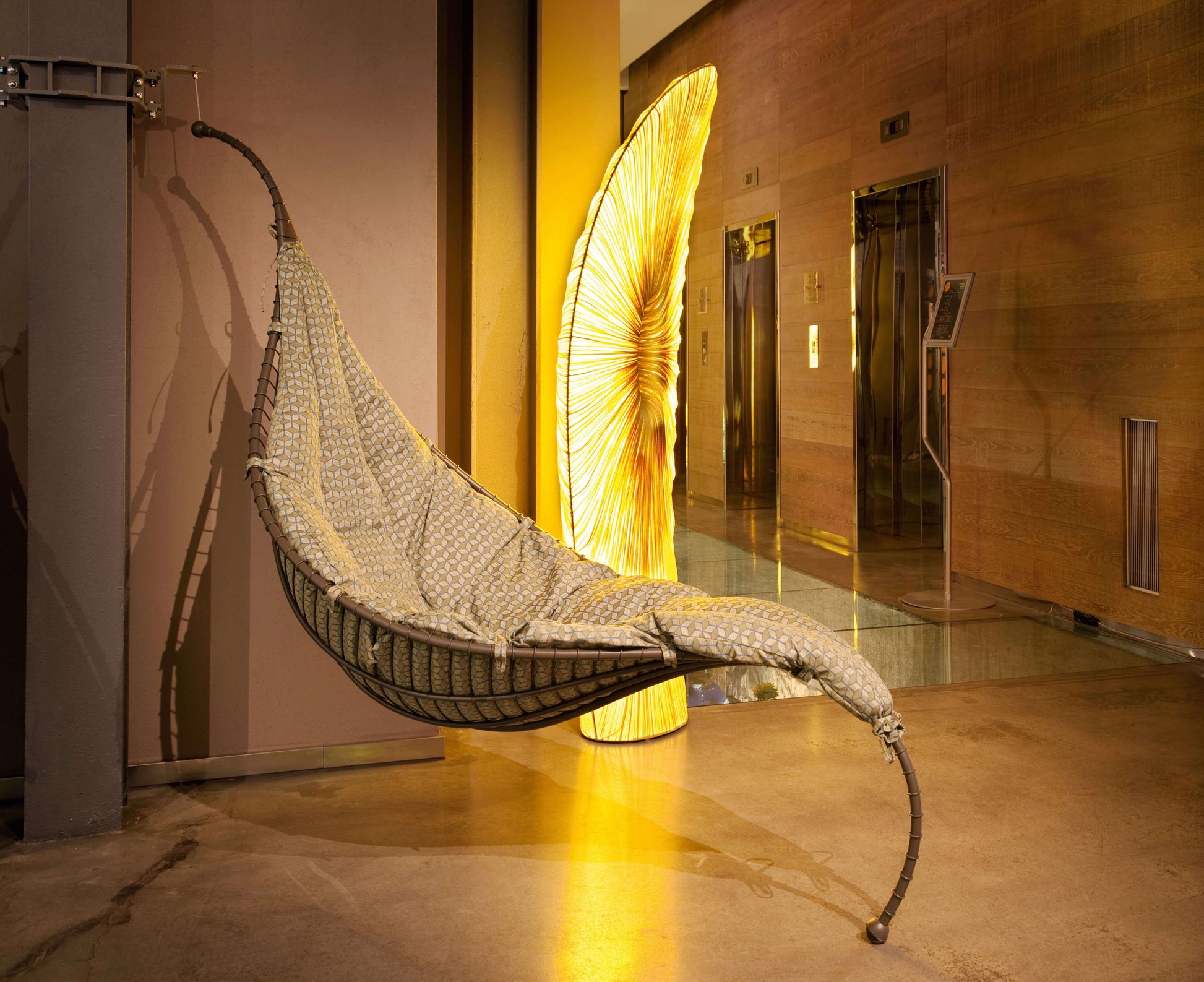 Hanging chair in a modern indoor setting with a large decorative light in the background.