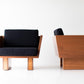 Two modern chairs with wooden frames and black cushions on a white background