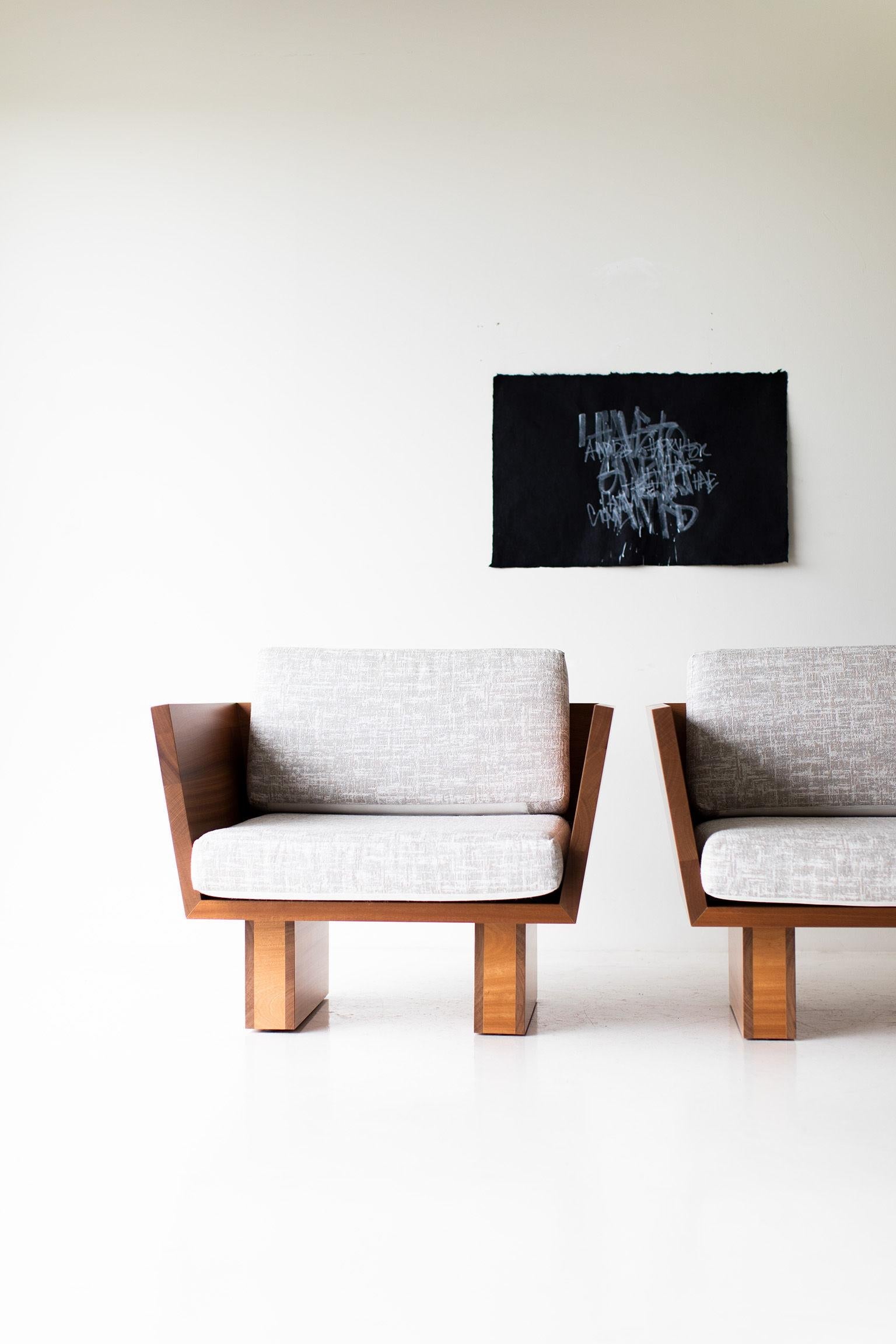 Two modern chairs with wooden frames and white cushions against a white wall with a black framed picture.