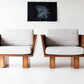 Two modern chairs with wooden frames and gray cushions in a minimalistic room.