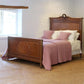 Wooden bed with pink blanket and pillows in a room with a window.