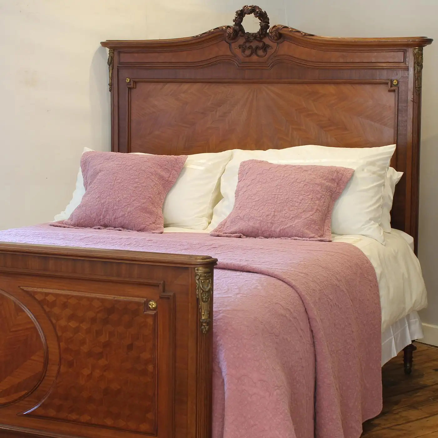 Bed with wooden headboard and pink bedding in a room.