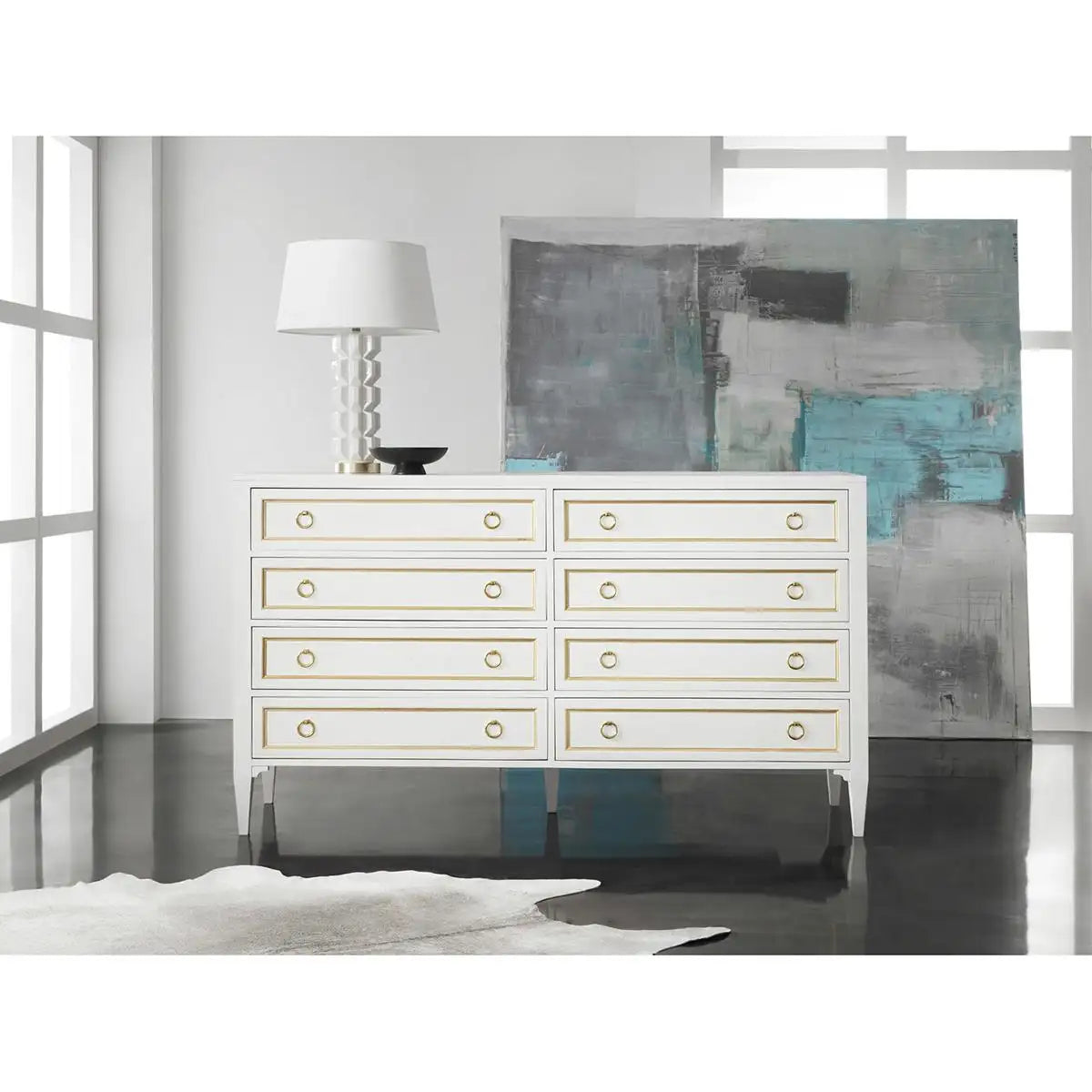 White dresser with gold accents in a room with abstract art and a lamp.