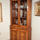 Wooden corner cabinet with decorative plates inside, against a light-colored wall.