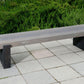Long wooden bench on a paved area with greenery in the background
