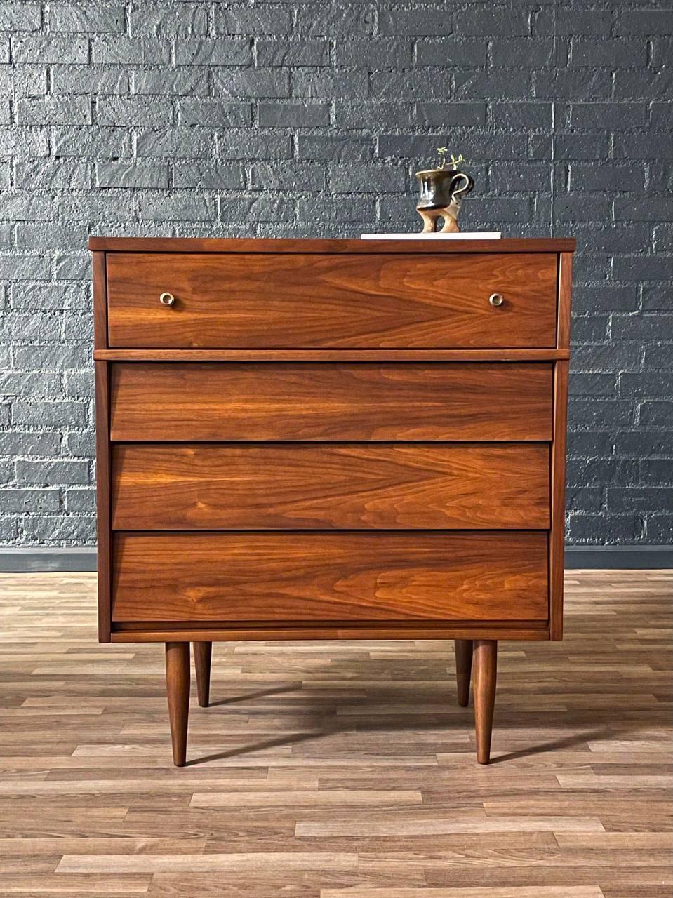 Wooden dresser with three drawers against a gray brick wall.