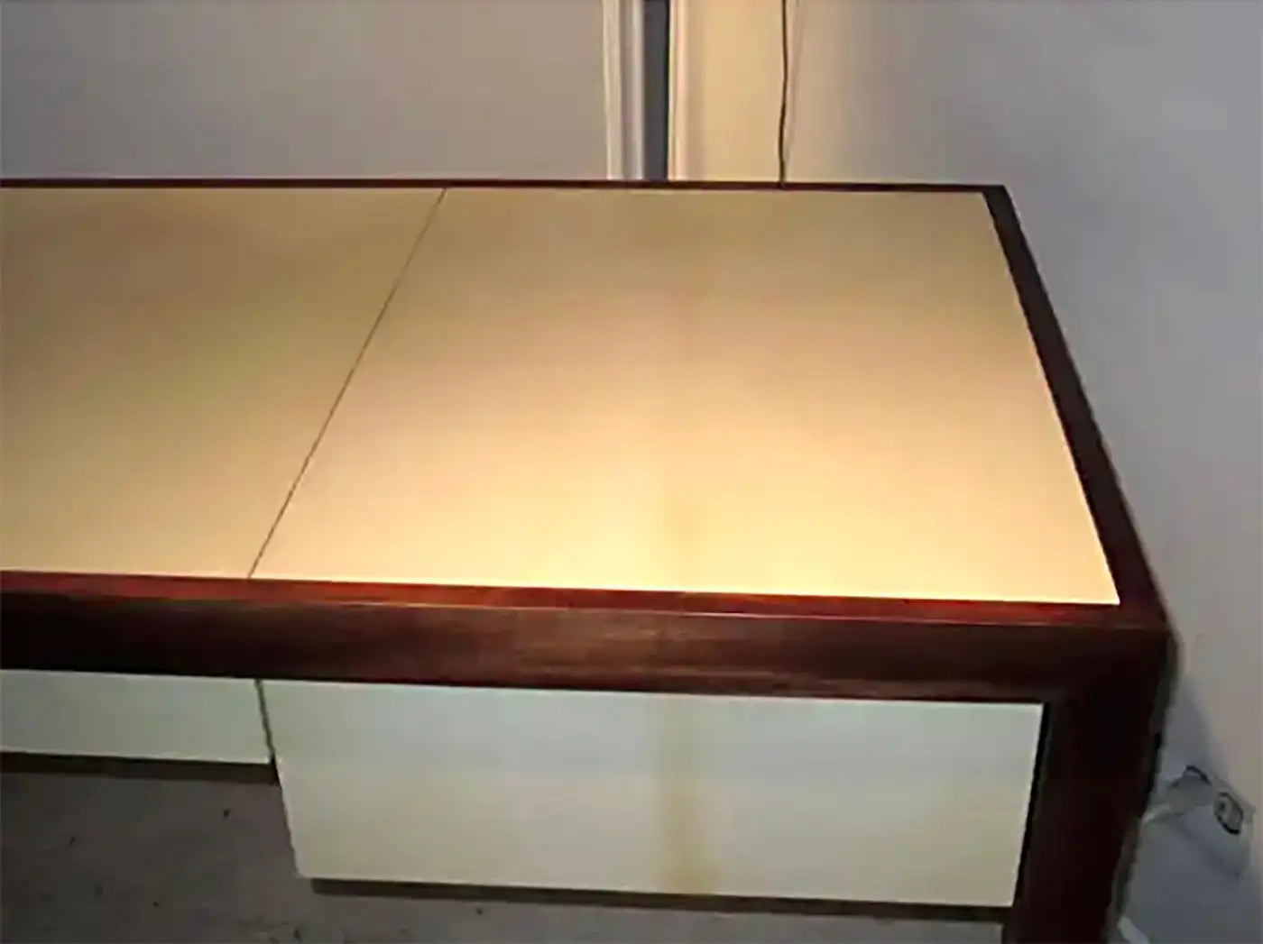 Wooden desk with a beige top against a plain wall