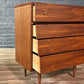 Wooden dresser with three drawers against a gray brick wall.
