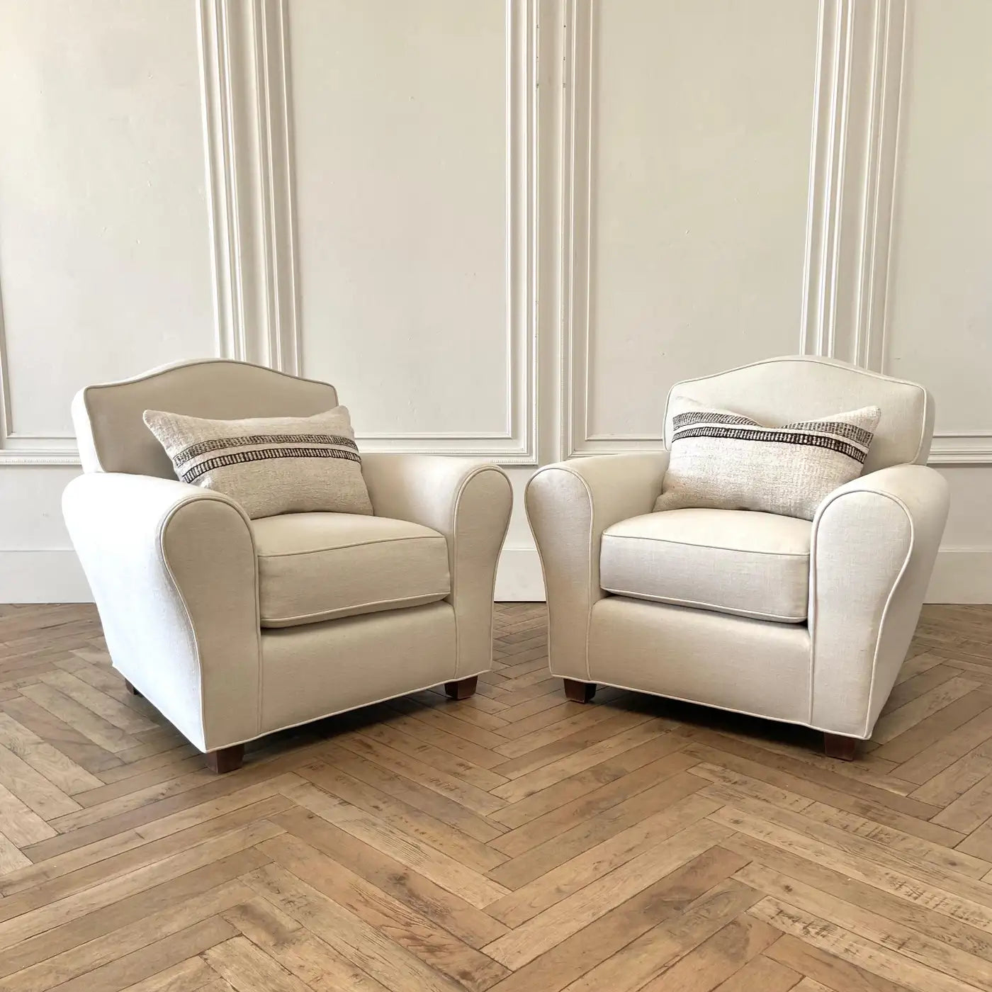Two beige armchairs with striped cushions on a wooden floor.