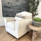 White armchair with decorative pillows in a room with a wooden floor and a plant.
