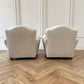 Two beige armchairs on a wooden floor with white walls.
