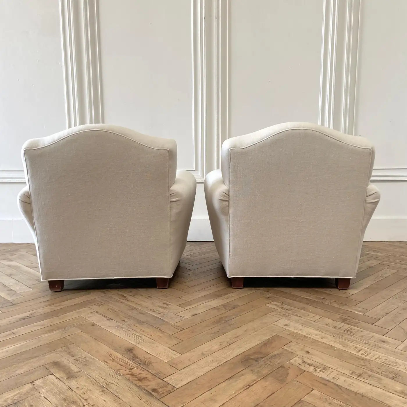 Two beige armchairs on a wooden floor with white walls.