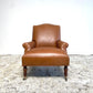 Brown leather armchair on a textured floor with a white wall background