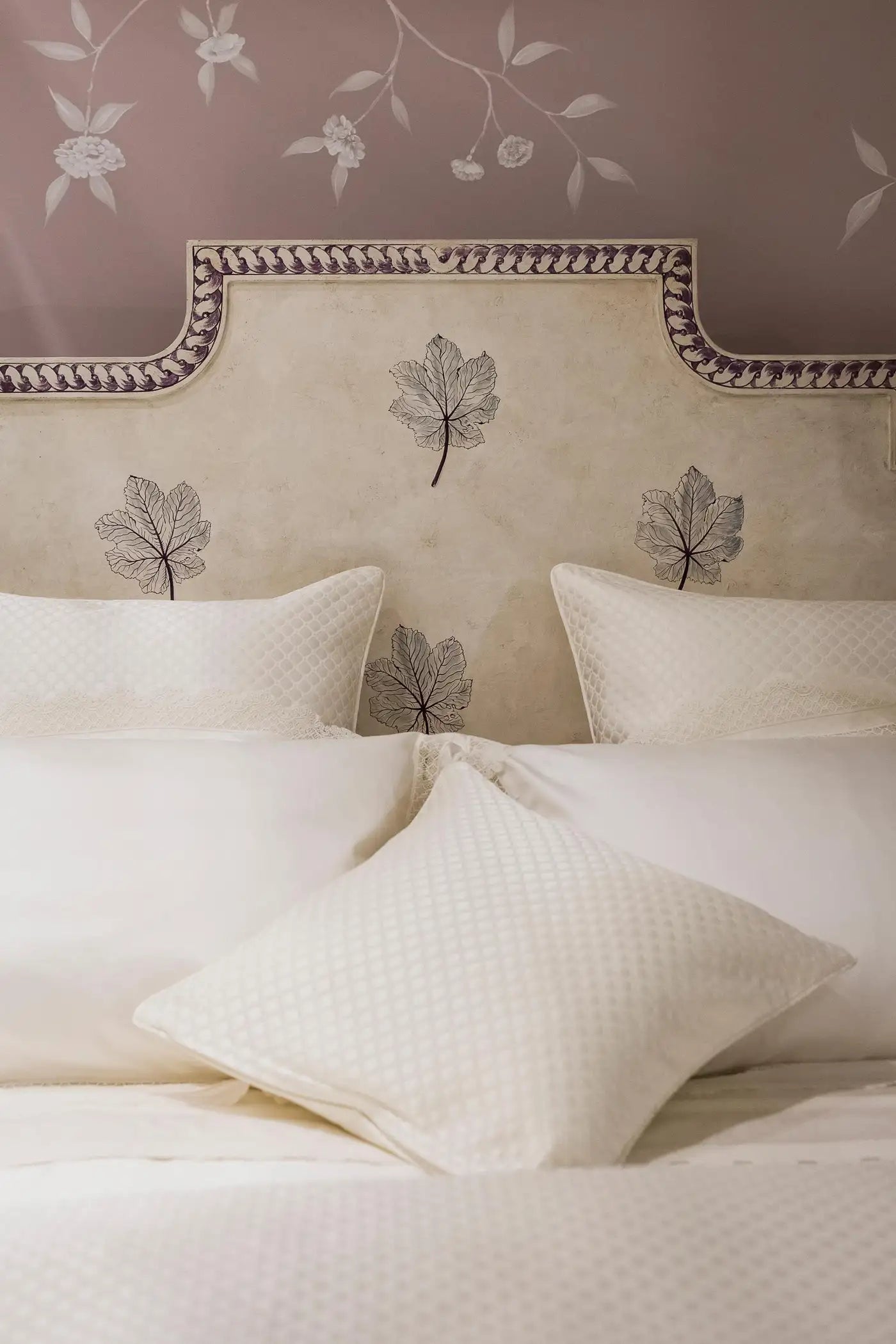 Beige headboard with leaf patterns and matching pillows on a bed.