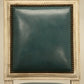 Teal upholstered chair with decorative frame against a beige wall