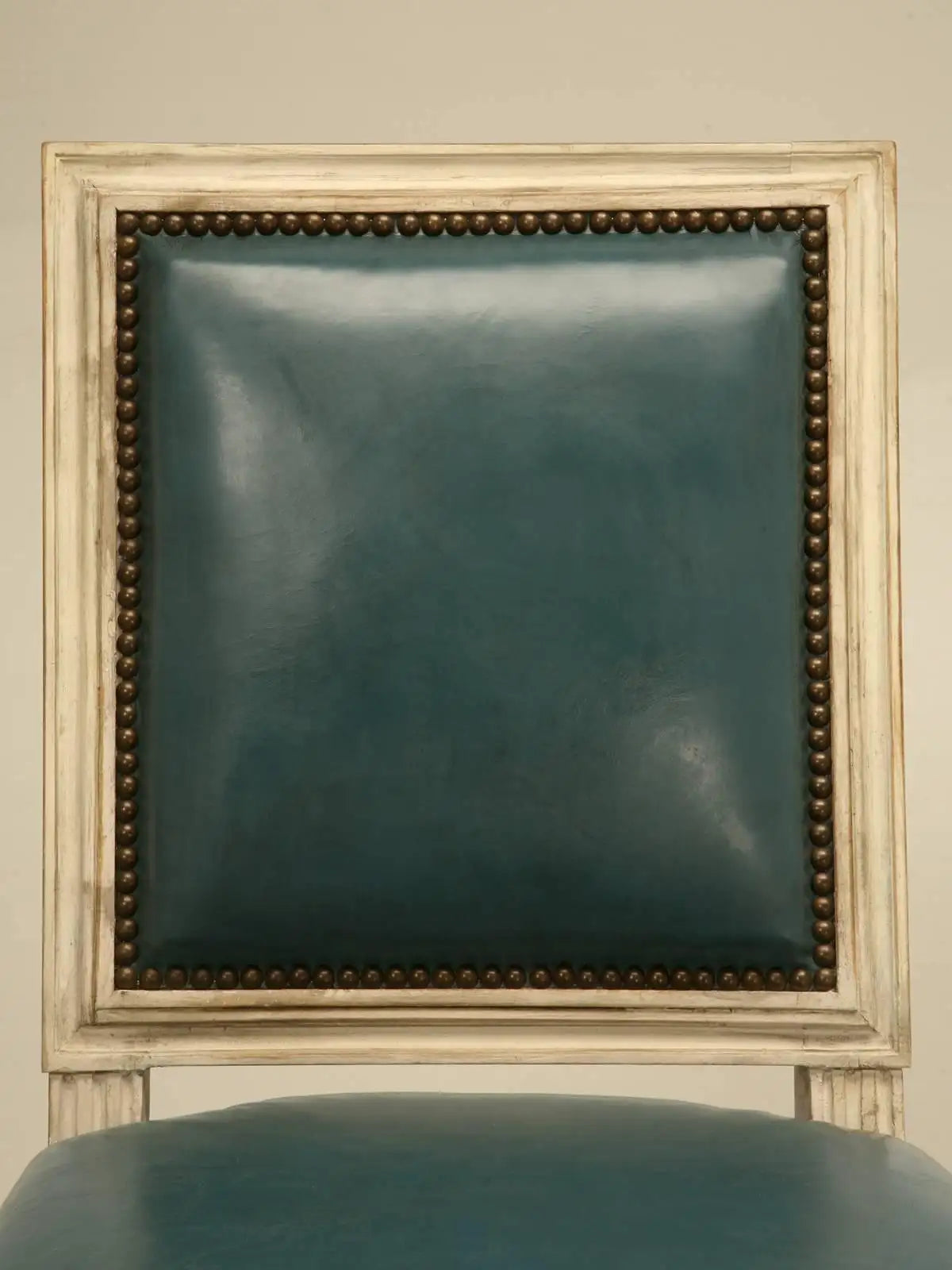 Teal upholstered chair with decorative frame against a beige wall