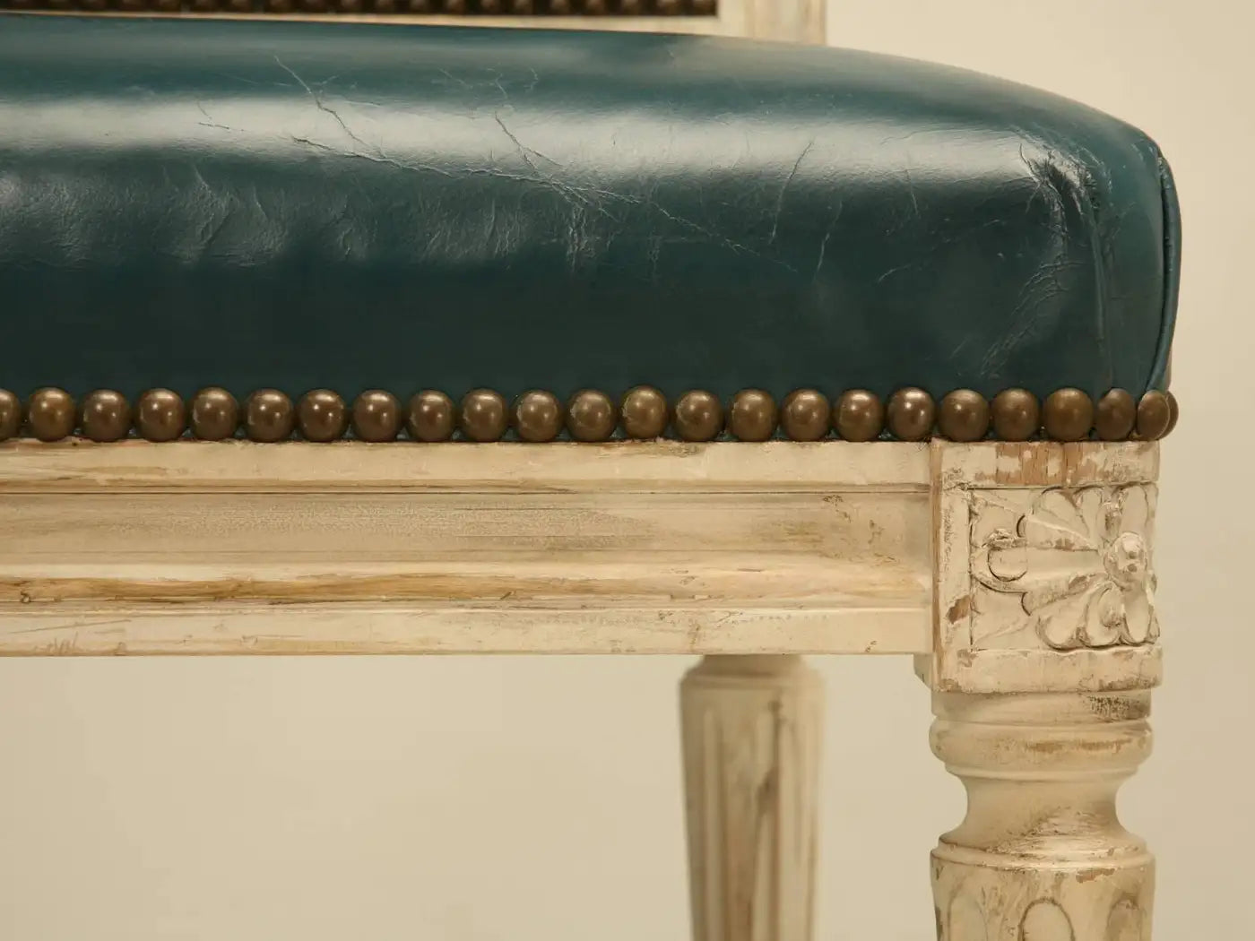 Vintage chair with green leather seat and brass nailhead trim on a beige background