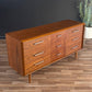 Wooden dresser with multiple drawers on a wooden floor against a dark wall.